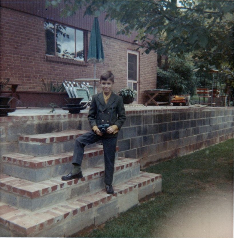 A boy in a jacket and tie holding a camera on brick steps, Arlington, Virginia, 1970s