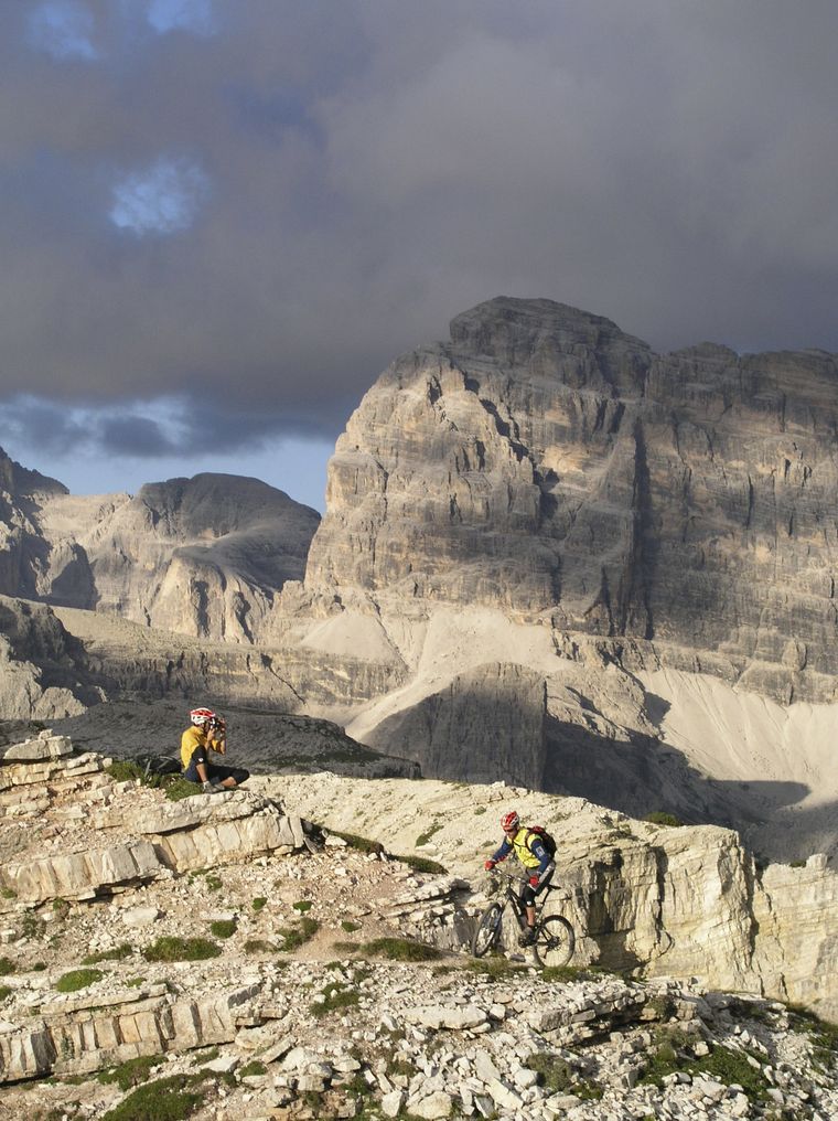 A photographer shooting a mountain biker on a limestone ledge below the Tre Cime